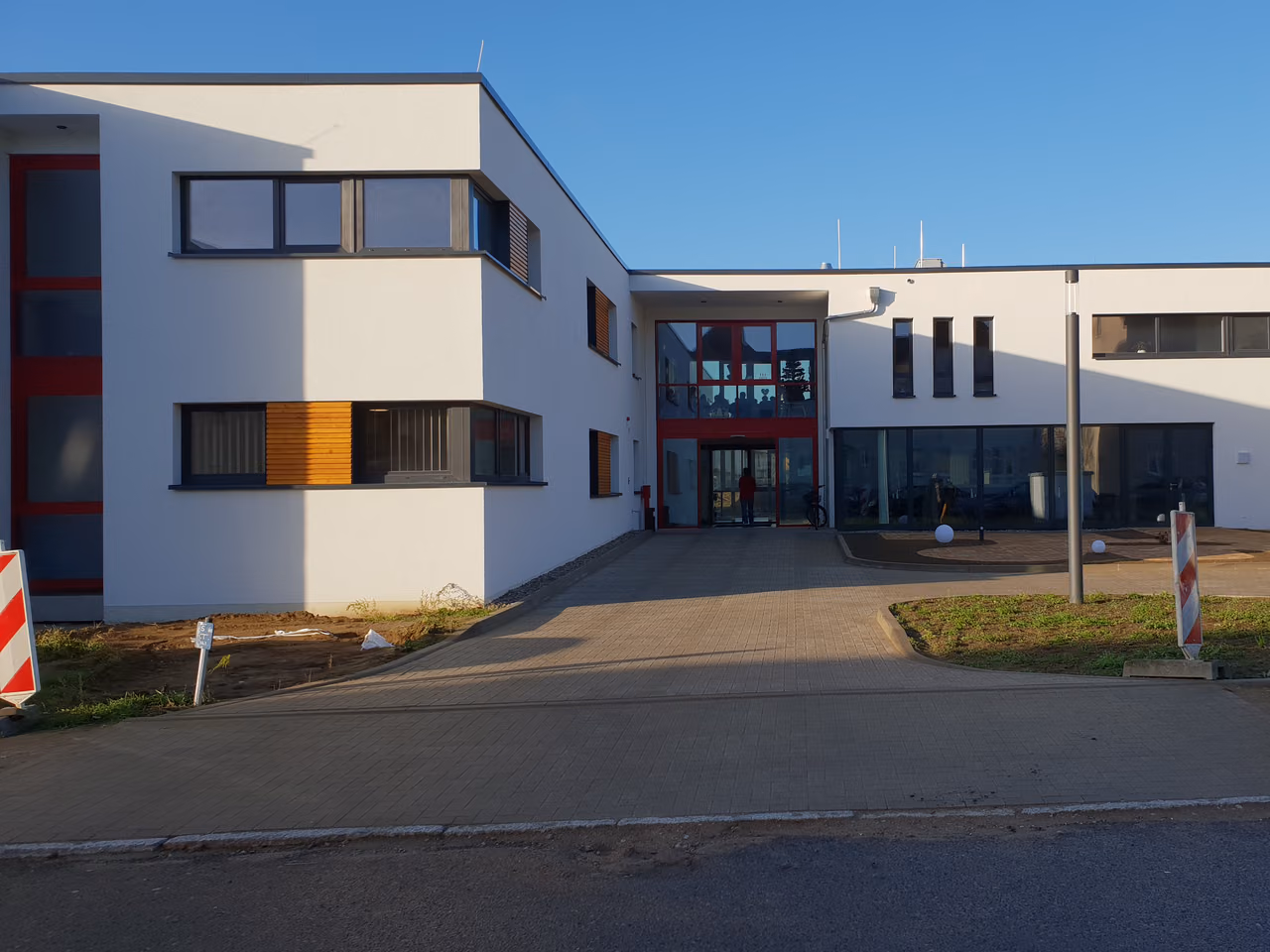 Eingang des Pflegeheims: verglaster Eingangsbau mit roten Rahmen zwischen zwei weißen Flachdachbauten